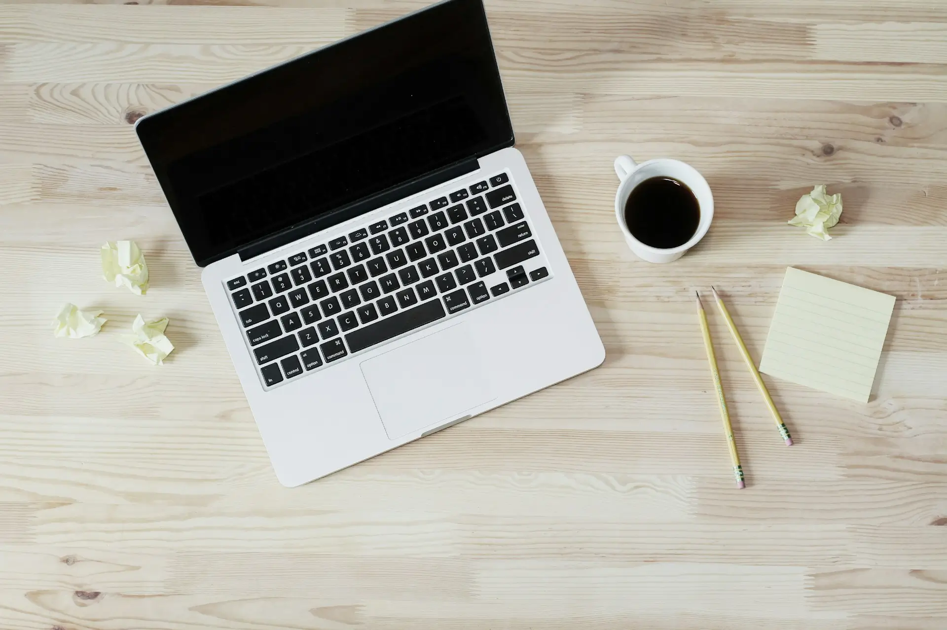 Laptop with coffee, pencils, and notes on a wooden desk representing workspace and planning at Niotechone